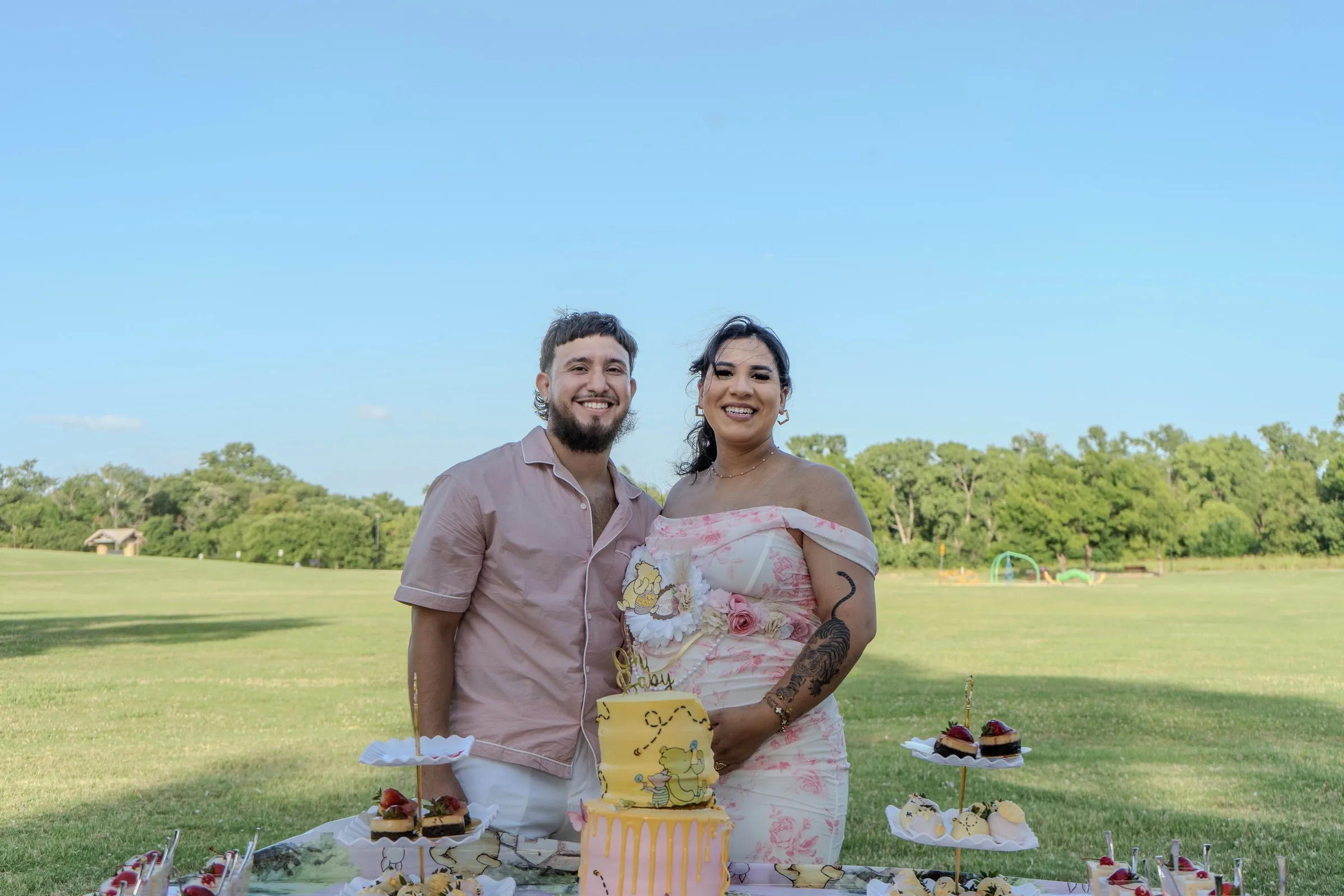 A couple stands behind a dessert table in an open park field at golden hour