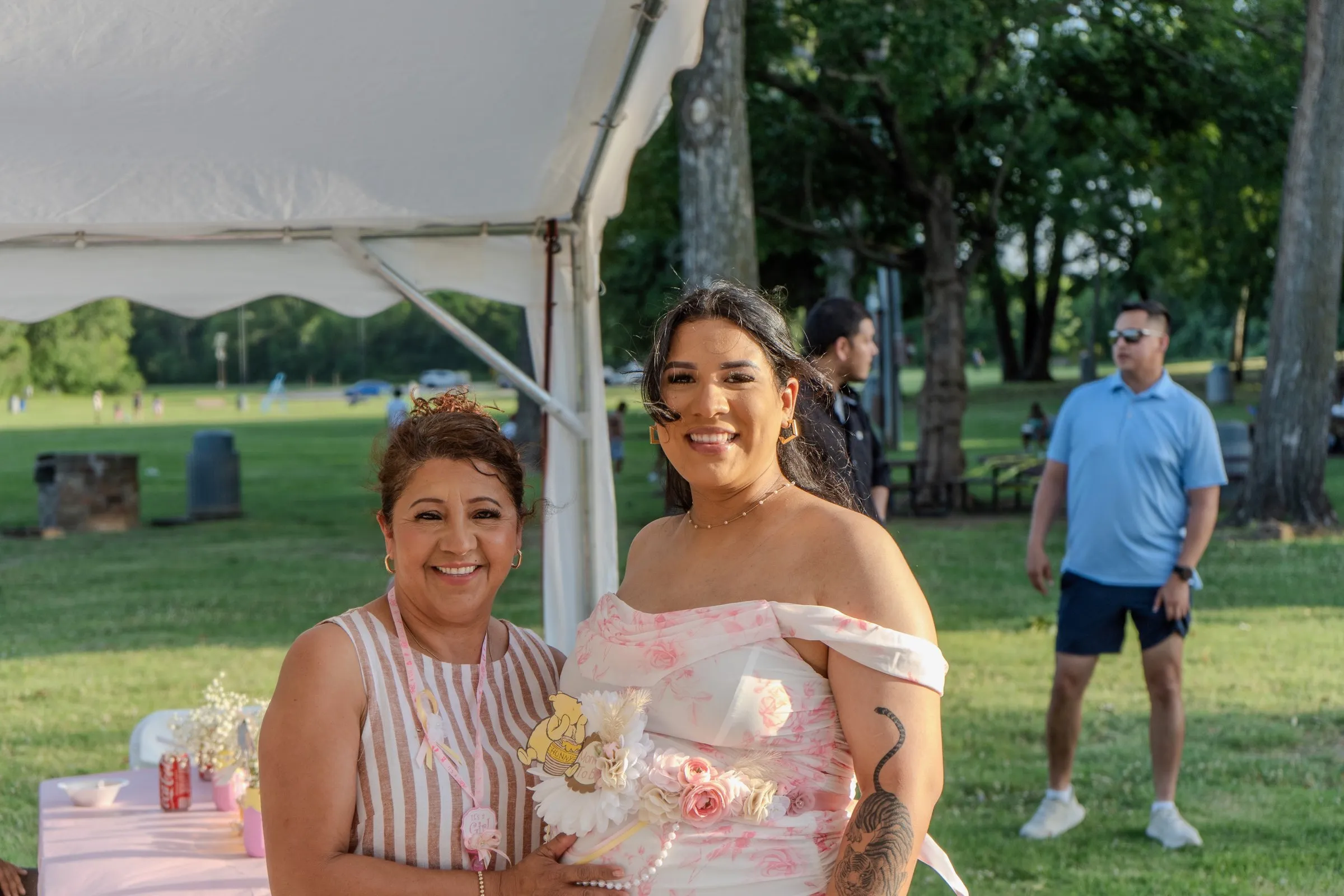 A mother and daughter pose together at an outdoor shower, a tent behind them