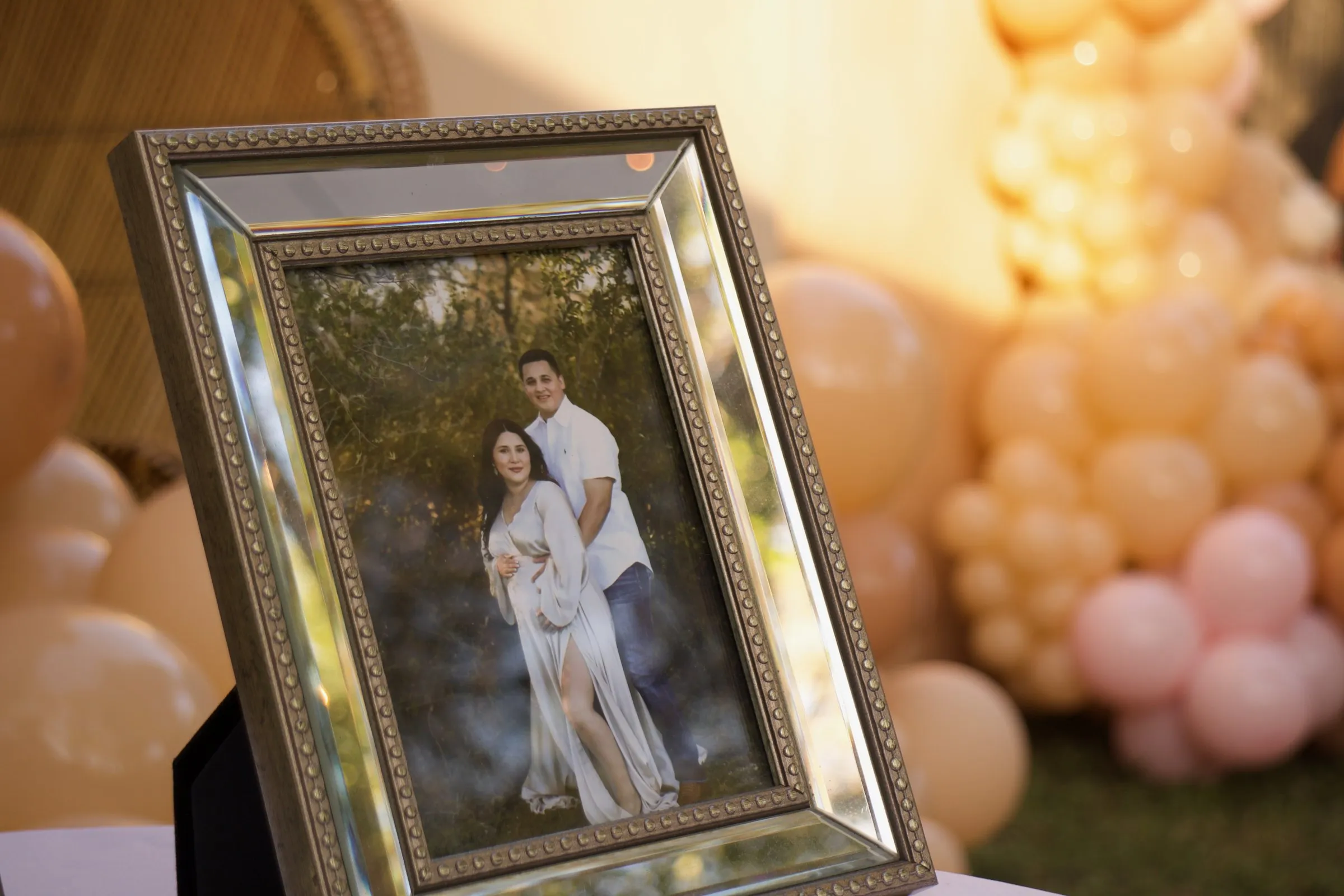 A framed maternity portrait on a table, balloons soft in the background
