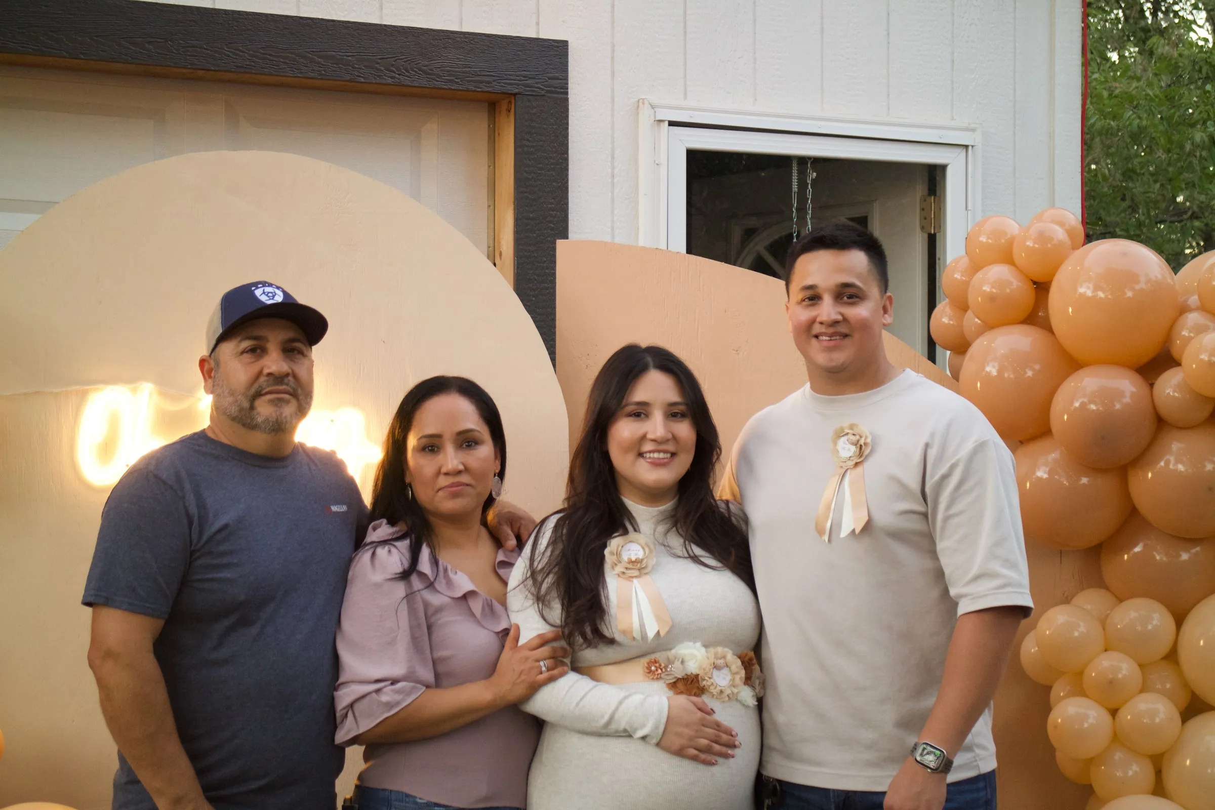 A family of four poses in front of a balloon arch at a baby shower