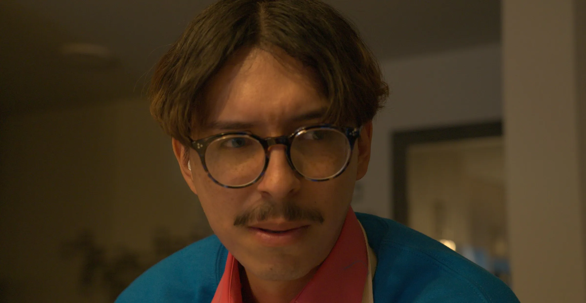 Close-up of a mustached man in glasses and a blue jacket